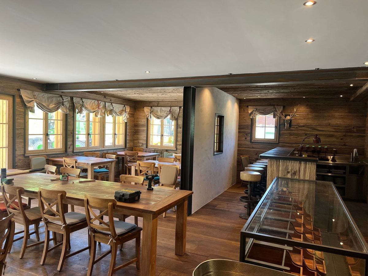 Chaletruimte van JUMPlan in Saanen met teak tafels, teak stoelen met kruis en de bar op de achtergrond