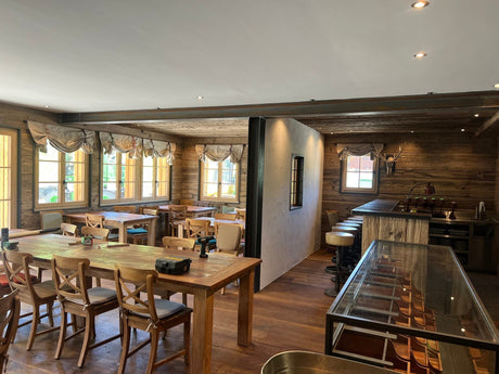 Chaletruimte van JUMPlan in Saanen met teak tafels, teak stoelen met kruis en de bar op de achtergrond